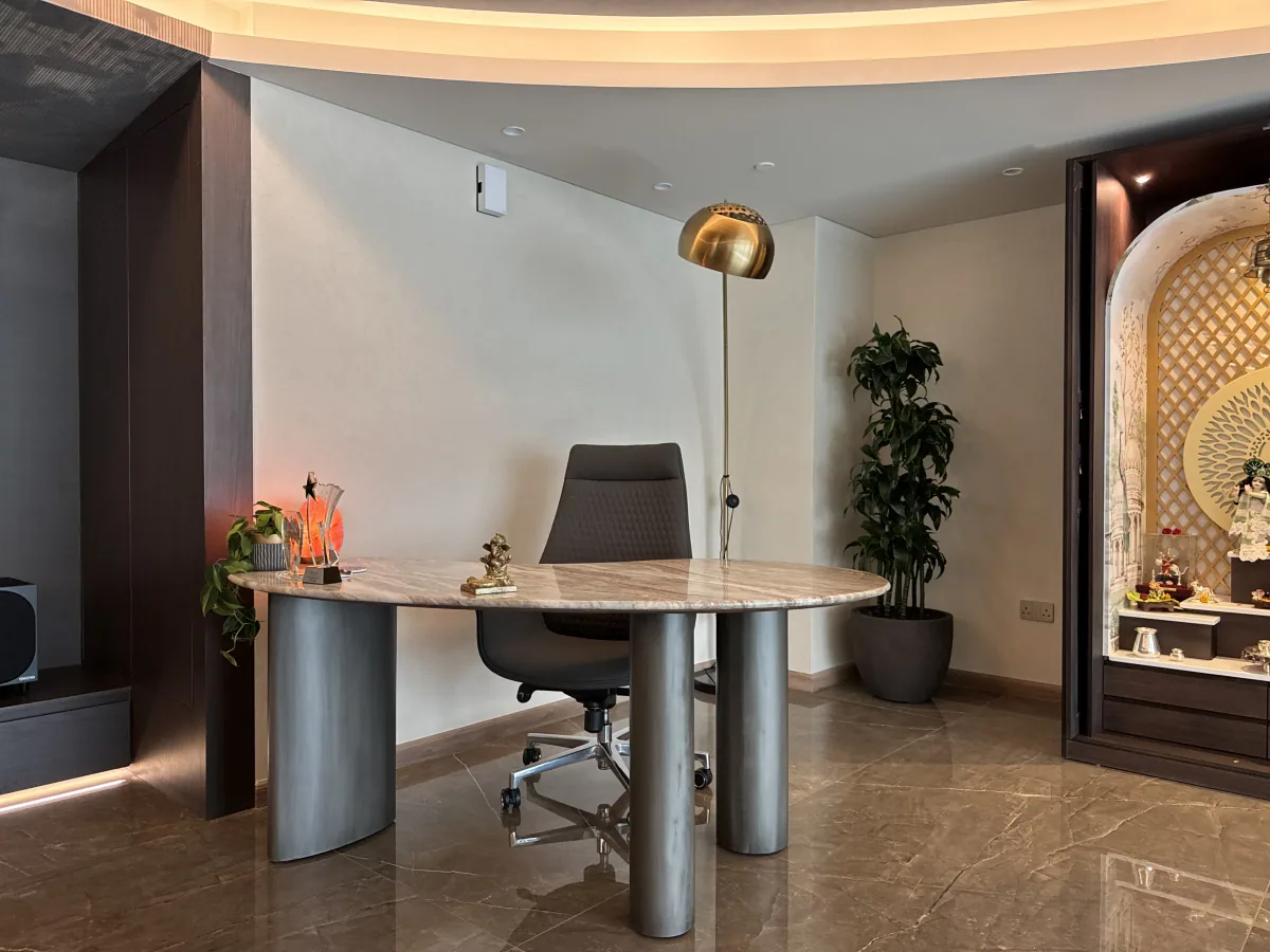 Private study with a stone oval desk, dark timber joinery and a lit feature niche